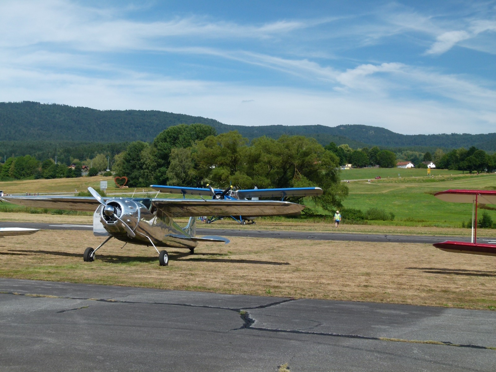 Poliertes silbernes Flugzeug am Boden, dahinter die blaue Antonow An-2