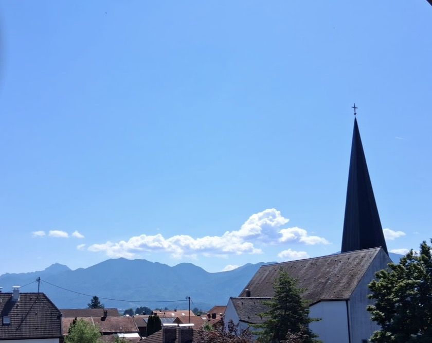 Dunkler Kirchturm vor blauem Himmel und der Bergkette am Horizont